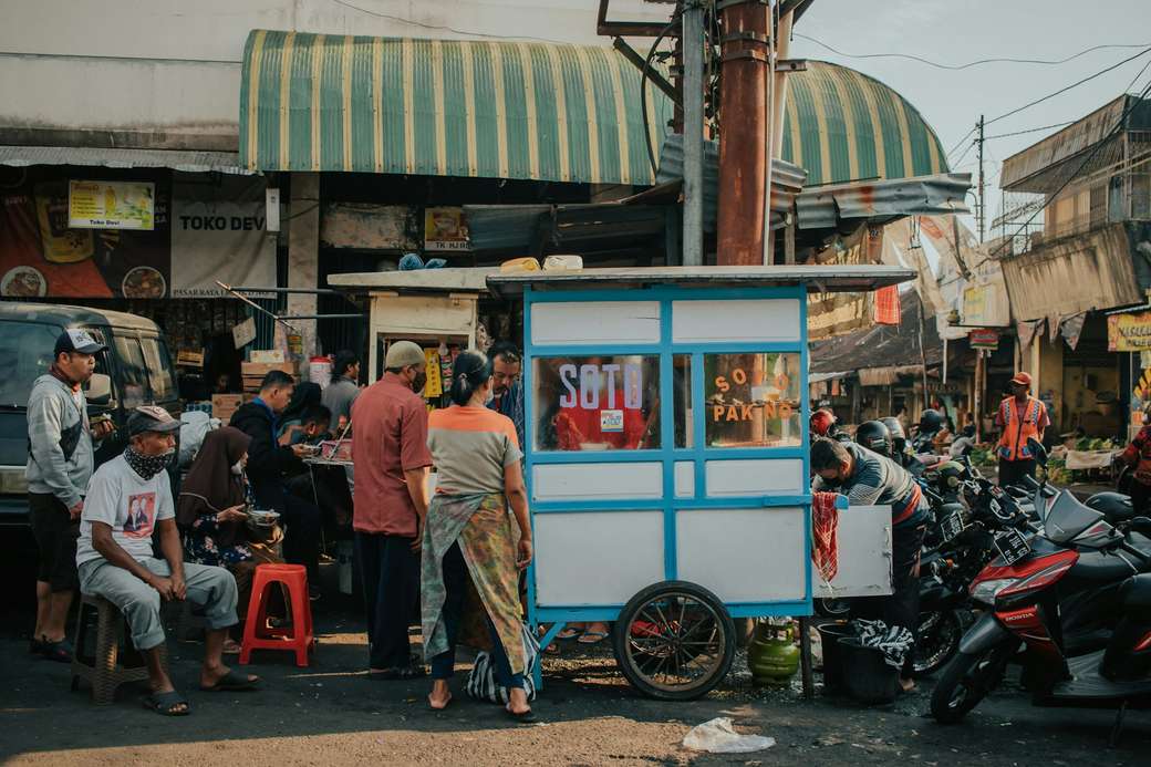 Customers gathered around a soto cart on a street corner in Indonesia, with motorbikes parked alongside.