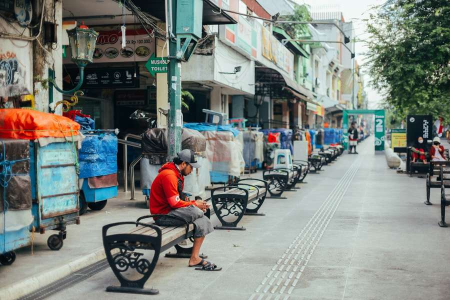 A quiet morning on Malioboro street in Yogyakarta, with shopfronts, benches and a man sitting on one of them.